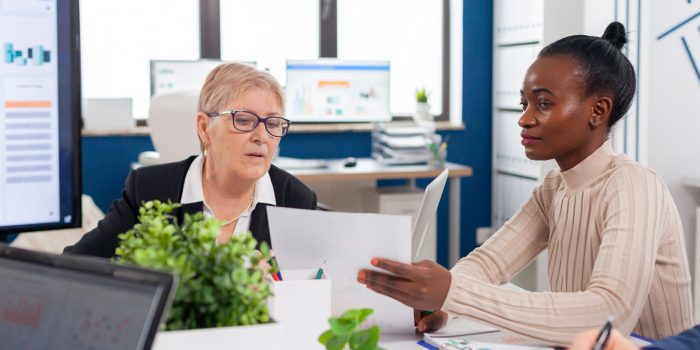 African employee in financial business board meeting room talking with senior entrepreneur investors looking analysing project documents. Personal colleagues of startup.